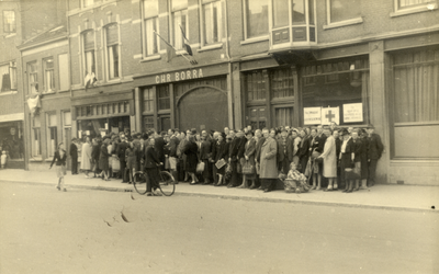 97583 Afbeelding van een rij mensen voor de kruidenierswinkel van de Fa. K. Achterberg (Burgemeester Reigerstraat 27) ...